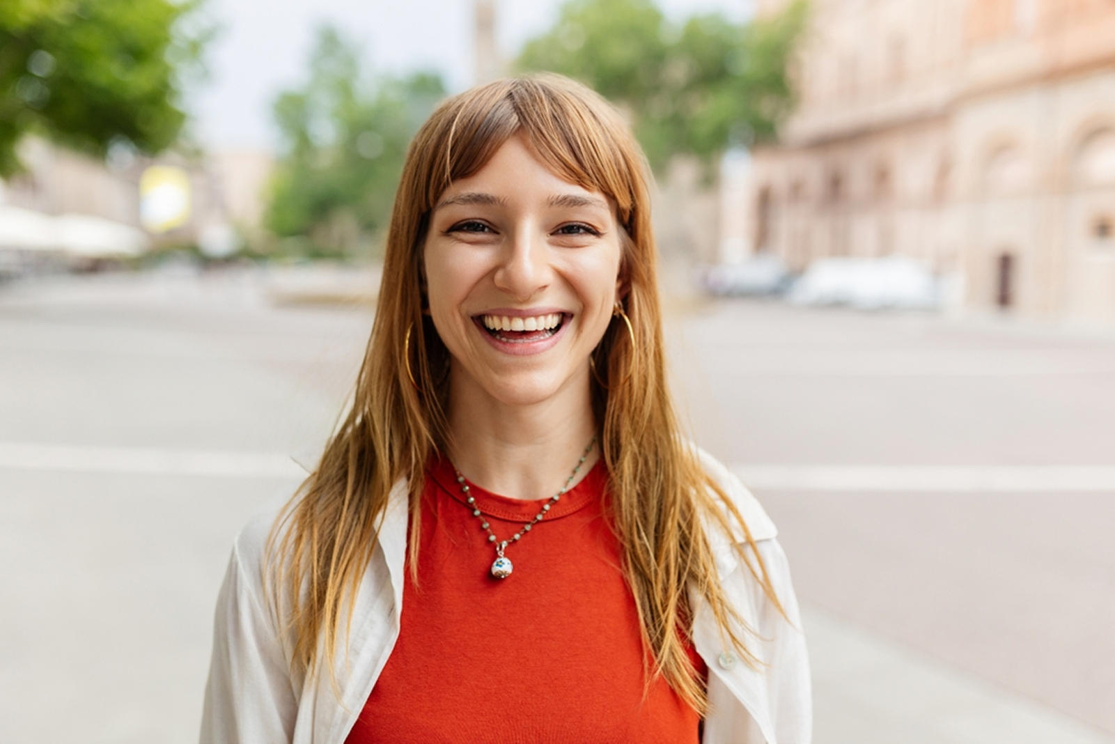 A smiling woman stands in the street, exuding joy and positivity in her surroundings.