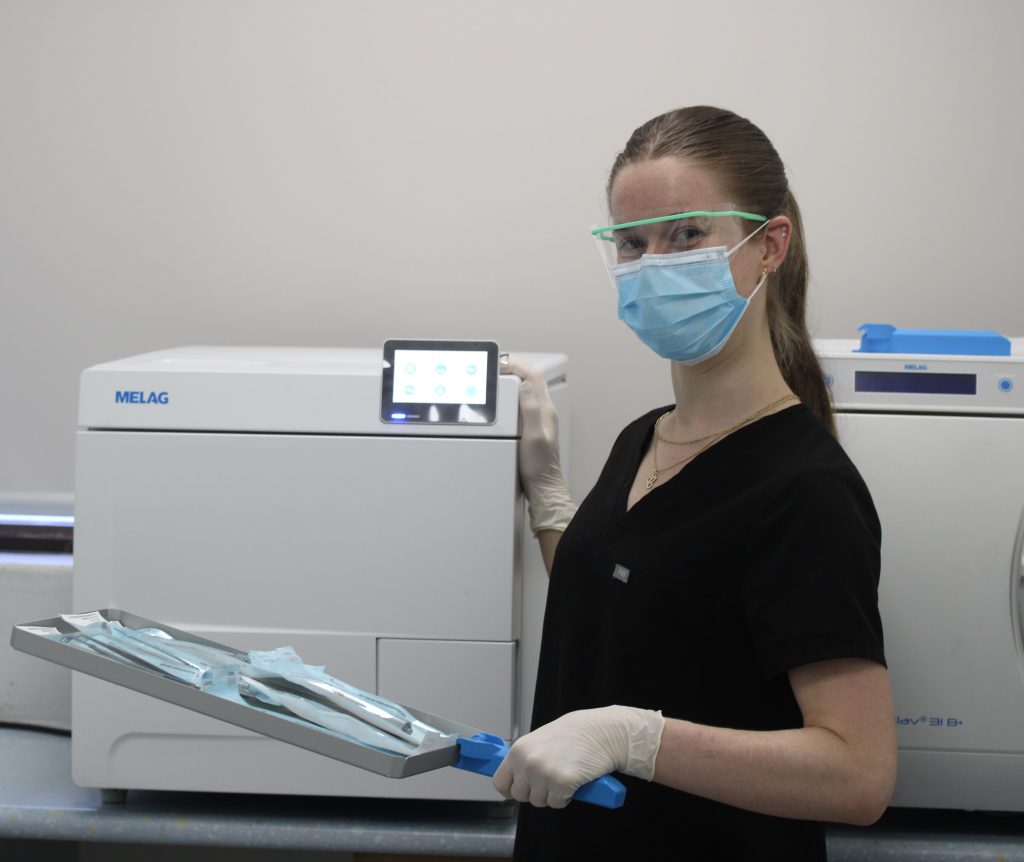 A woman in a mask and gloves holds a tray, prepared for serving or handling food safely.