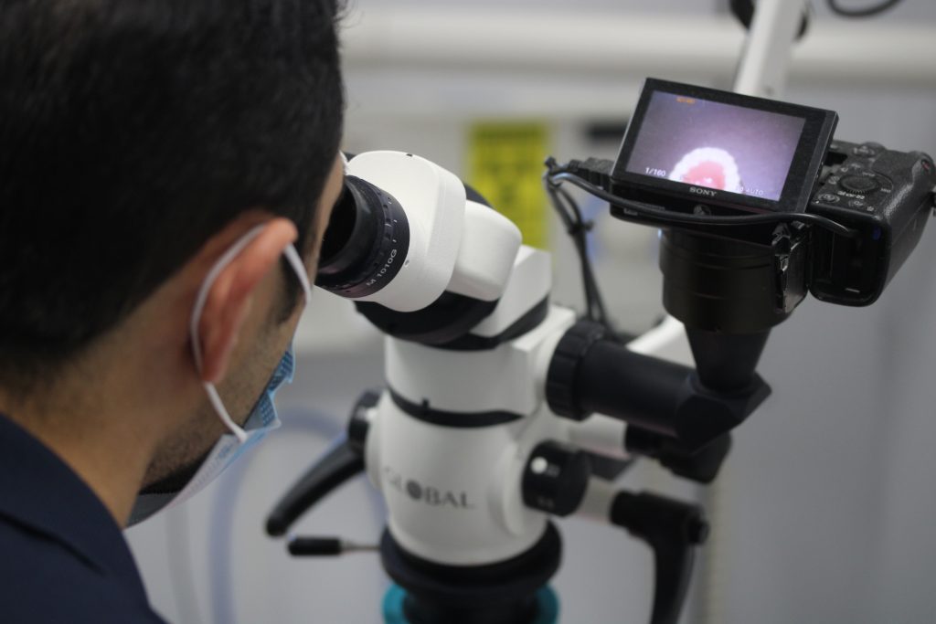 A man peers intently through a microscope, examining a specimen on the slide.